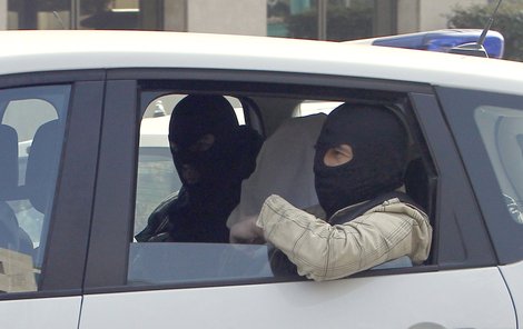 Abdelkader se zakrytým obličejem mezi policisty.