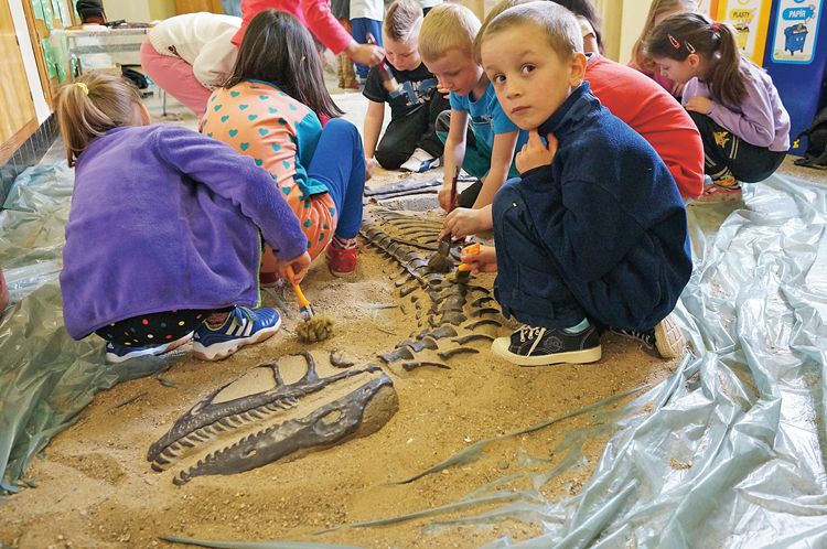 V rámci Mobilního triloparku děti vyhrabávají maketu kostry dinosaura Deinonychus